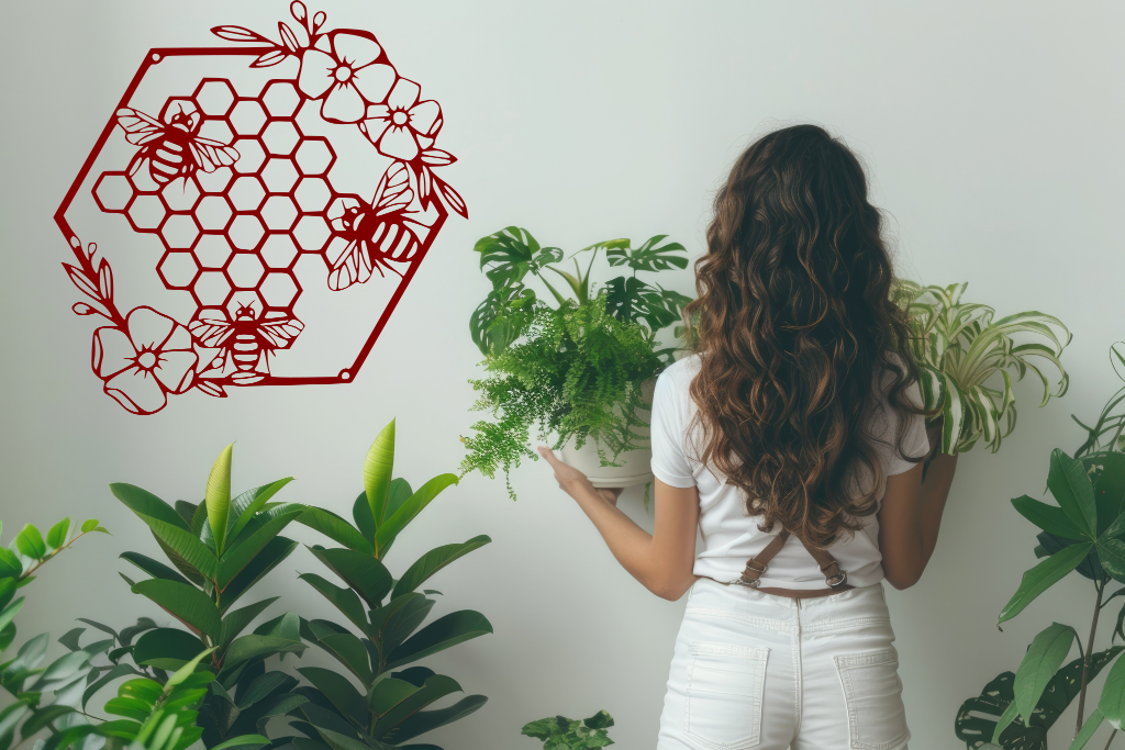 Metal wall art featuring three bees hovering over a floral honeycomb pattern, finished in Manor Red powder coating, mounted on a light-colored wall, complementing indoor plants and creating a nature-inspired decor.