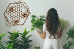 Metal wall art featuring three bees hovering over a floral honeycomb pattern, finished in Rust Patina powder coating, mounted on a light-colored wall, complementing indoor plants and creating a nature-inspired decor.