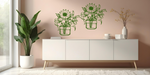 Metal wall art set featuring two jars filled with blooming flowers, including sunflowers and lilies, finished in Mistletoe powder coating, mounted on a soft pink wall above a modern white cabinet, creating a cheerful and nature-inspired interior decor.