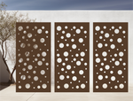 Metal privacy screen with a modern bubble pattern of varying circle sizes, finished in Rust Patina powder coating, displayed outdoors against a white wall, providing both privacy and an artistic element to the space.