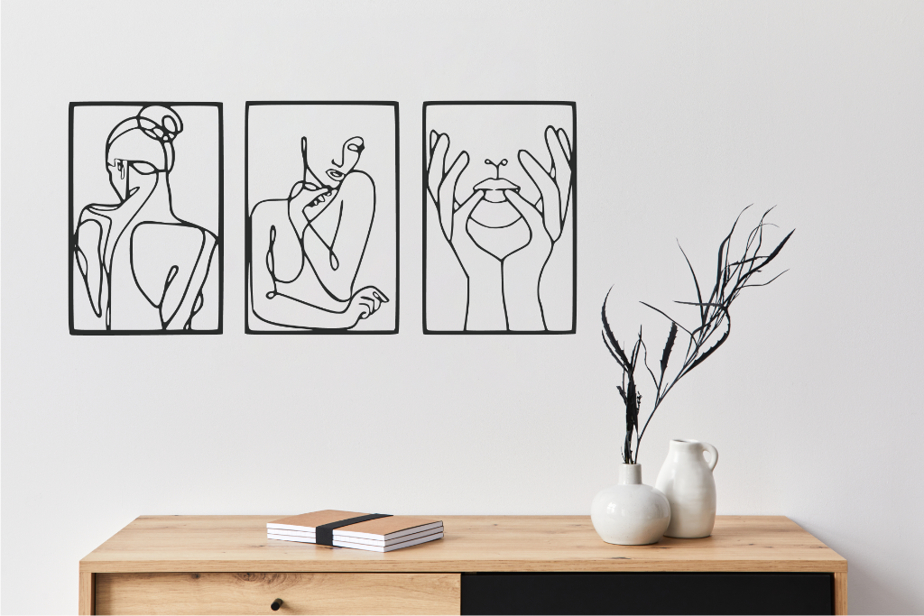 Metal wall art set featuring three minimalist line-drawing silhouettes of feminine figures in graceful poses, finished in Night Sky Matt Black powder coating, mounted on a white wall above a natural wood console, adding an elegant and artistic touch to modern interiors.