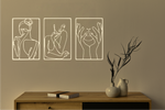 Metal wall art set featuring three minimalist line-drawing silhouettes of feminine figures in graceful poses, finished in Canola Cream powder coating, mounted on a white wall above a natural wood console, adding an elegant and artistic touch to modern interiors.