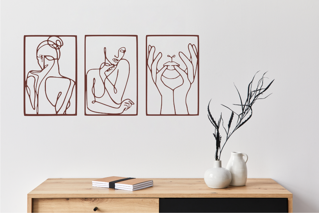 Metal wall art set featuring three minimalist line-drawing silhouettes of feminine figures in graceful poses, finished in Manor Red powder coating, mounted on a white wall above a natural wood console, adding an elegant and artistic touch to modern interiors.