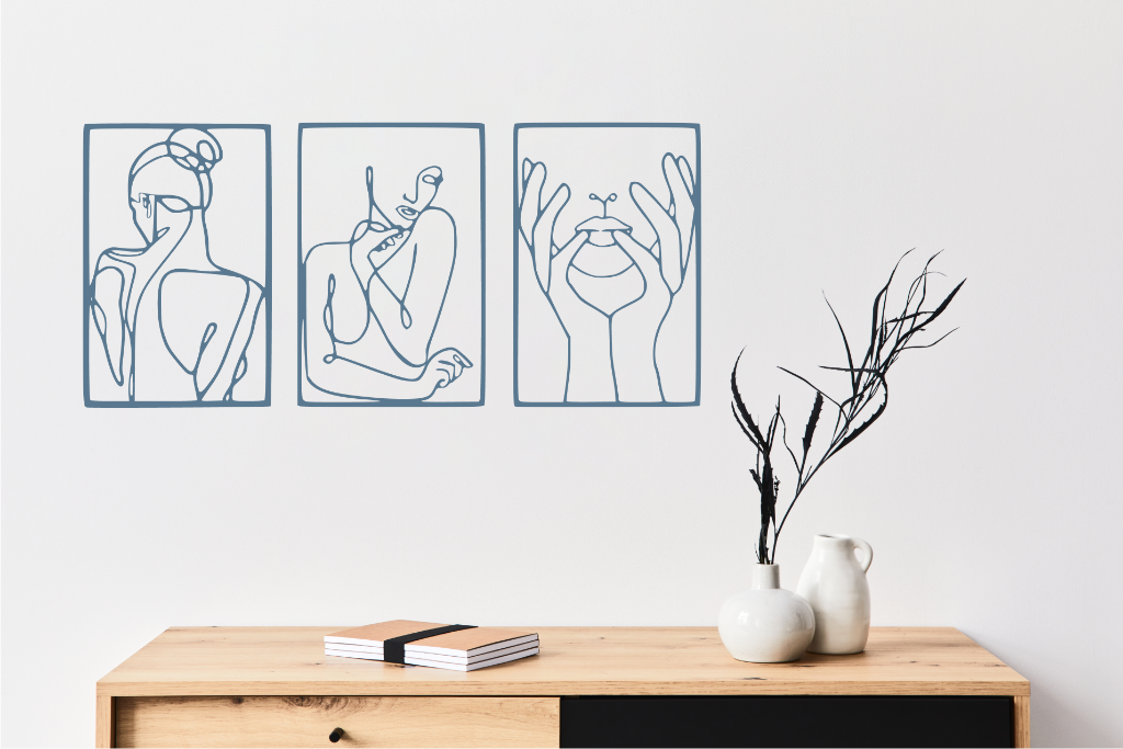 Metal wall art set featuring three minimalist line-drawing silhouettes of feminine figures in graceful poses, finished in Wedgwood Satin powder coating, mounted on a white wall above a natural wood console, adding an elegant and artistic touch to modern interiors.