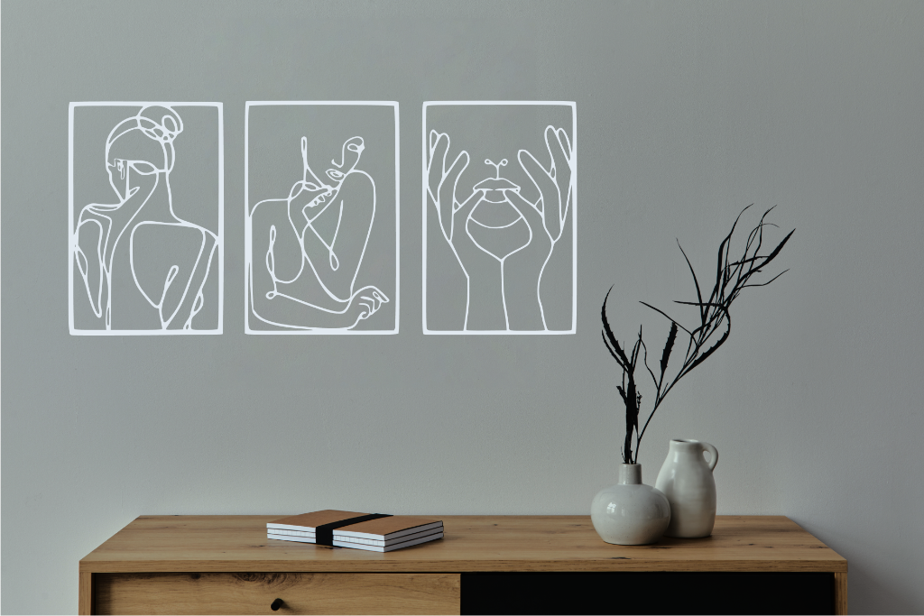 Metal wall art set featuring three minimalist line-drawing silhouettes of feminine figures in graceful poses, finished in Bright White Gloss powder coating, mounted on a white wall above a natural wood console, adding an elegant and artistic touch to modern interiors.