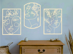 Set of three decorative metal wall art pieces, each featuring an abstract feminine face intertwined with floral elements, finished in Canola Cream powder coating. The artwork is displayed on a white wall above a wooden chest of drawers, adding a modern and artistic touch to the room.