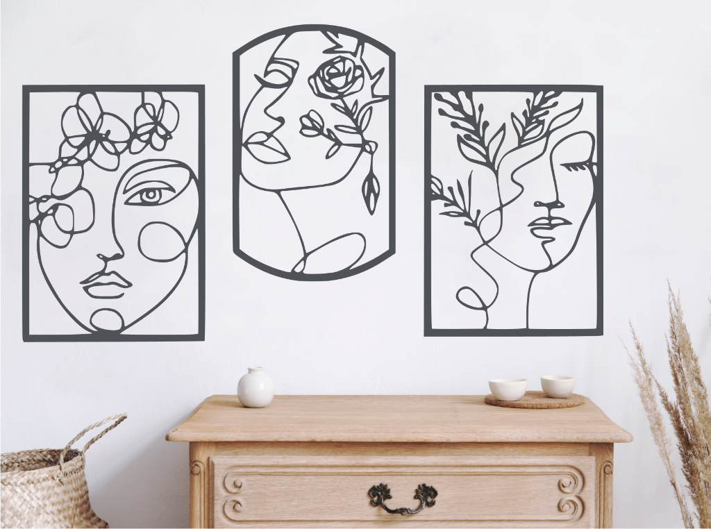 Set of three decorative metal wall art pieces, each featuring an abstract feminine face intertwined with floral elements, finished in Berry Grey Gloss powder coating. The artwork is displayed on a white wall above a wooden chest of drawers, adding a modern and artistic touch to the room.