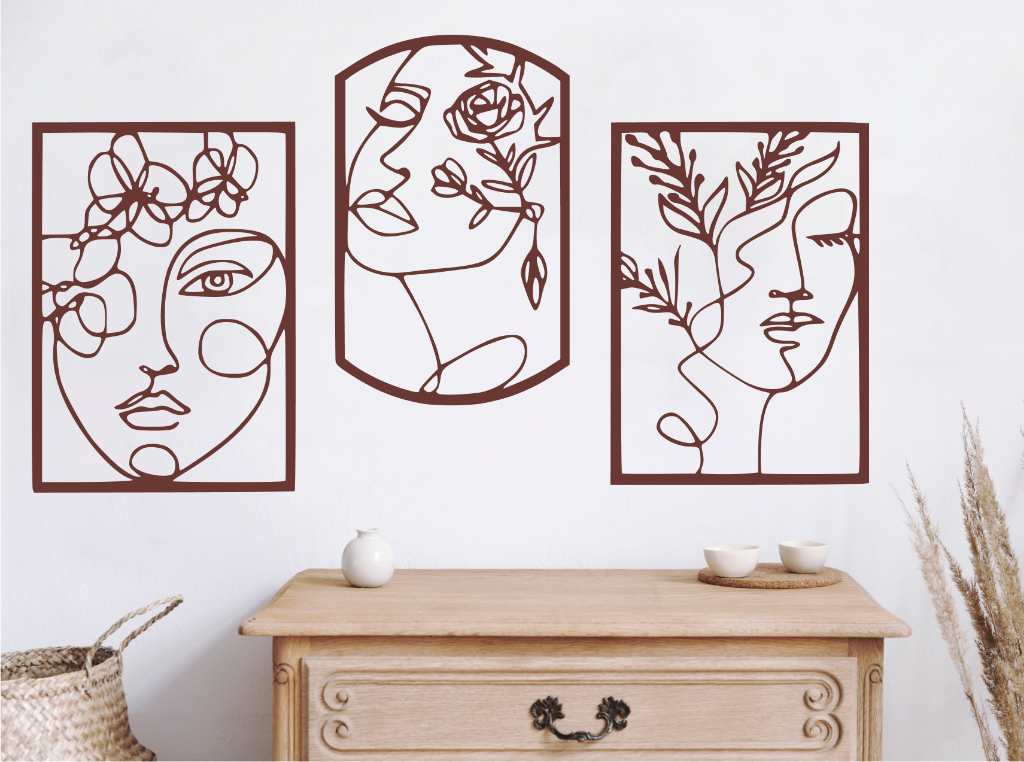 Set of three decorative metal wall art pieces, each featuring an abstract feminine face intertwined with floral elements, finished in Manor Red powder coating. The artwork is displayed on a white wall above a wooden chest of drawers, adding a modern and artistic touch to the room.