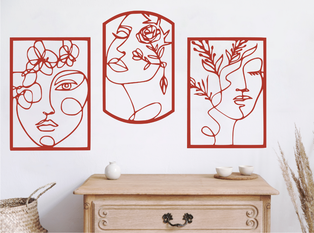 Set of three decorative metal wall art pieces, each featuring an abstract feminine face intertwined with floral elements, finished in Signal Red powder coating. The artwork is displayed on a white wall above a wooden chest of drawers, adding a modern and artistic touch to the room.