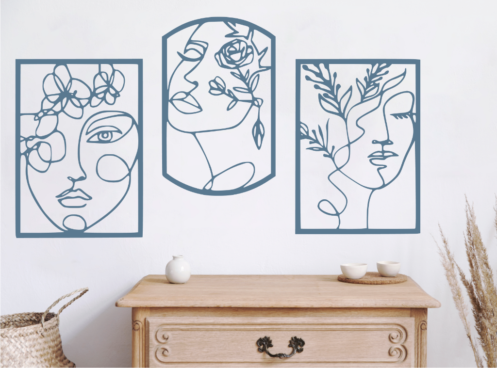 Set of three decorative metal wall art pieces, each featuring an abstract feminine face intertwined with floral elements, finished in Wedgwood Satin powder coating. The artwork is displayed on a white wall above a wooden chest of drawers, adding a modern and artistic touch to the room.