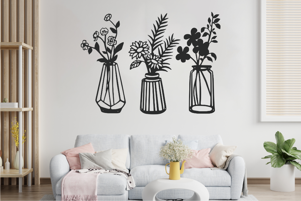 Set of three metal wall art pieces, each featuring a unique vase with blooming flowers, finished in Night Sky Matt Black powder coating. The artwork is displayed on a white wall above a cozy sofa, adding a delicate and artistic floral touch to the living room.