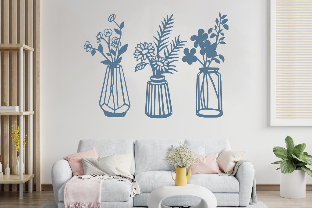 Set of three metal wall art pieces, each featuring a unique vase with blooming flowers, finished in Blaze Blue Gloss powder coating. The artwork is displayed on a white wall above a cozy sofa, adding a delicate and artistic floral touch to the living room.