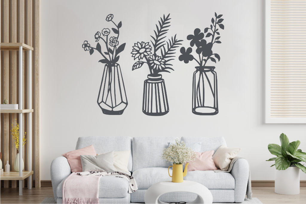 Set of three metal wall art pieces, each featuring a unique vase with blooming flowers, finished in Berry Grey Gloss powder coating. The artwork is displayed on a white wall above a cozy sofa, adding a delicate and artistic floral touch to the living room.