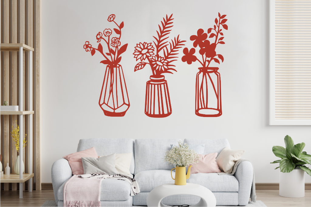 Set of three metal wall art pieces, each featuring a unique vase with blooming flowers, finished in Manor Red powder coating. The artwork is displayed on a white wall above a cozy sofa, adding a delicate and artistic floral touch to the living room.