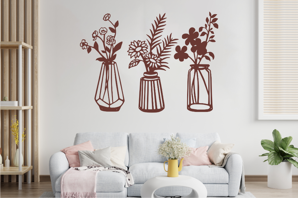 Set of three metal wall art pieces, each featuring a unique vase with blooming flowers, finished in Rust Patina powder coating. The artwork is displayed on a white wall above a cozy sofa, adding a delicate and artistic floral touch to the living room.