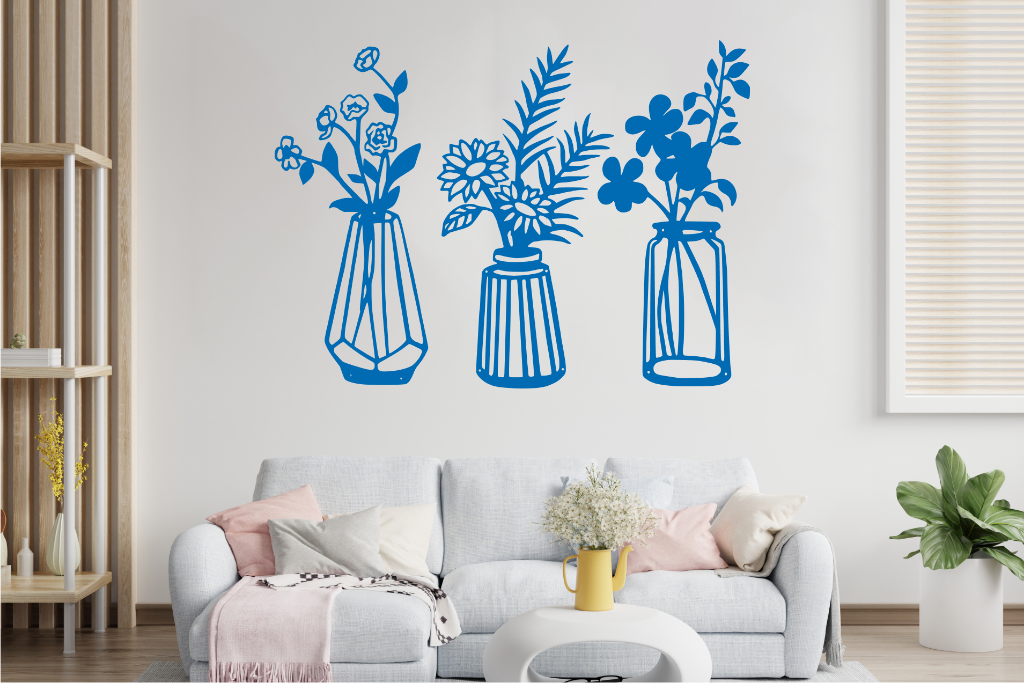 Set of three metal wall art pieces, each featuring a unique vase with blooming flowers, finished in Wedgwood Satin powder coating. The artwork is displayed on a white wall above a cozy sofa, adding a delicate and artistic floral touch to the living room.