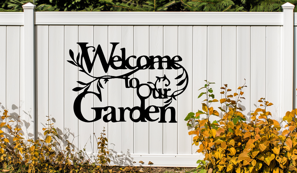 Metal wall art sign featuring the phrase 'Welcome to our Garden' with decorative branches and leaves integrated into the design, finished in Night Sky Matt Black powder coating. The sign is mounted on a white fence, adding a welcoming touch to an outdoor garden space.