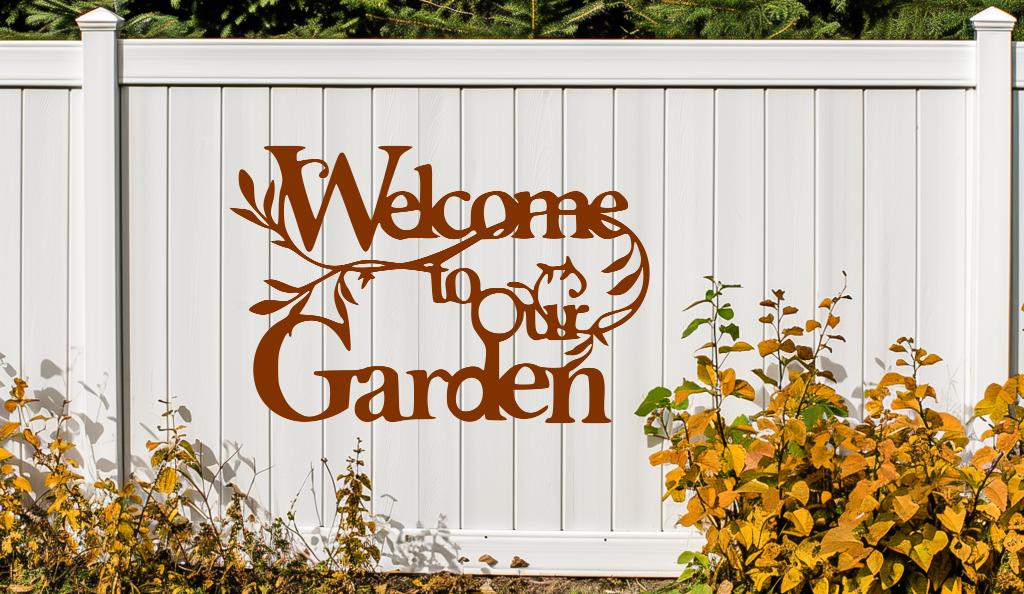 Metal wall art sign featuring the phrase 'Welcome to our Garden' with decorative branches and leaves integrated into the design, finished in Rust Patina powder coating. The sign is mounted on a white fence, adding a welcoming touch to an outdoor garden space.