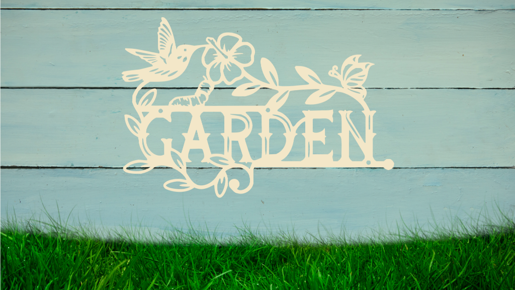 Metal wall art featuring the word 'GARDEN' with a decorative design of leaves, flowers, and a hummingbird, finished in Canola Cream powder coating, mounted on a white wooden wall above a patch of green grass, adding a welcoming and natural touch to outdoor garden spaces.