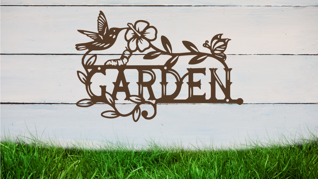 Metal wall art featuring the word 'GARDEN' with a decorative design of leaves, flowers, and a hummingbird, finished in Night Sky Matt Black powder coating, mounted on a white wooden wall above a patch of green grass, adding a welcoming and natural touch to outdoor garden spaces.