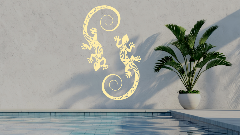 Metal wall art featuring two geckos with intricate detailing on their bodies, finished in Canola Cream powder coating, mounted on a light wall near a poolside, adding a tropical and playful touch to the outdoor space.