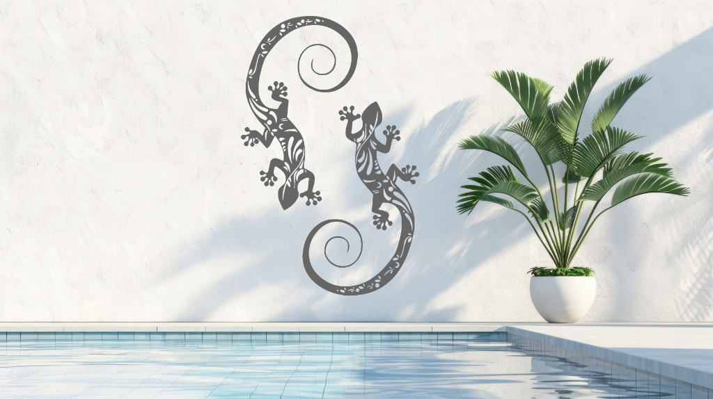 Metal wall art featuring two geckos with intricate detailing on their bodies, finished in Berry Grey Gloss powder coating, mounted on a light wall near a poolside, adding a tropical and playful touch to the outdoor space.