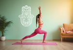 Decorative Hamsa hand metal wall art in Bright White Gloss, mounted on a pastel green wall next to a yoga enthusiast in a warrior pose.