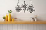 Metal wall art featuring three hanging planters with intricate plant designs, finished in Night Sky Matt Black powder coating, mounted on a kitchen wall. The piece brings a natural and modern aesthetic to the space, complementing the vibrant yellow decor elements on the counter below.