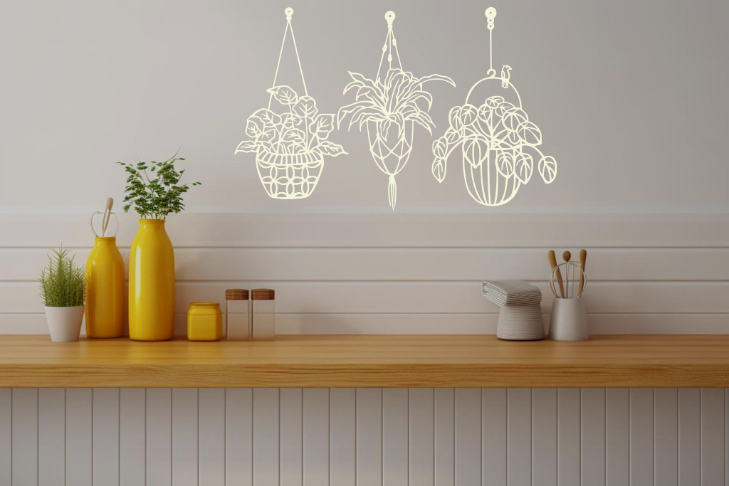 Metal wall art featuring three hanging planters with intricate plant designs, finished in Canola Cream powder coating, mounted on a kitchen wall. The piece brings a natural and modern aesthetic to the space, complementing the vibrant yellow decor elements on the counter below.