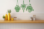 Metal wall art featuring three hanging planters with intricate plant designs, finished in Mistletoe powder coating, mounted on a kitchen wall. The piece brings a natural and modern aesthetic to the space, complementing the vibrant yellow decor elements on the counter below.