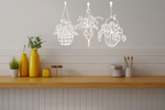 Metal wall art featuring three hanging planters with intricate plant designs, finished in Bright White Gloss powder coating, mounted on a kitchen wall. The piece brings a natural and modern aesthetic to the space, complementing the vibrant yellow decor elements on the counter below.