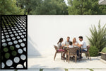 Modern metal privacy screen with a gradient of circular cut-outs, finished in Night Sky Matt Black, adding contemporary elegance to an outdoor dining space while offering privacy.