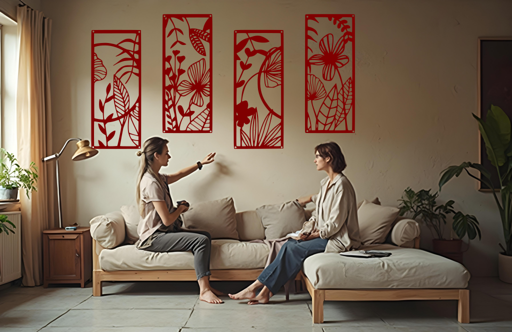 A four-piece metal wall art set from the 'Lush Escape Collection,' featuring intricate nature-inspired designs of leaves and flowers, finished in Manor Red powder coating. The artwork is mounted on a living room wall above a neutral-toned sofa, adding a calming and organic touch to the space.