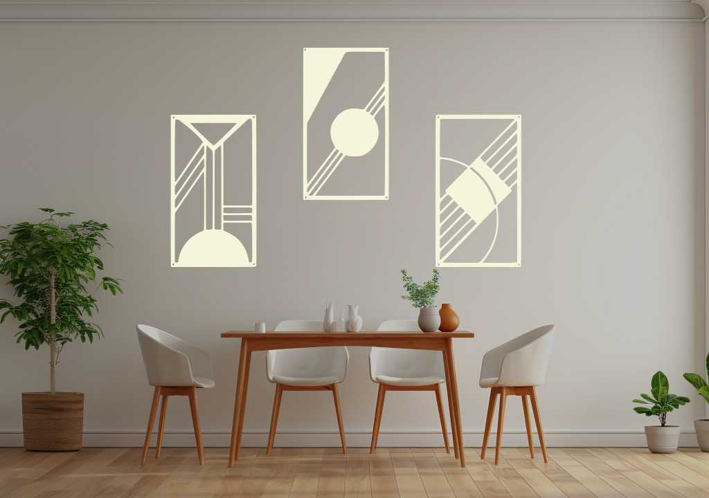 A three-piece minimalist metal wall art set from the 'Serenity in Simplicity' collection, featuring geometric designs of clean lines and abstract shapes, finished in Canola Cream powder coating. The artwork is mounted on a dining room wall above a simple wooden table with white chairs, creating a modern and calming aesthetic.