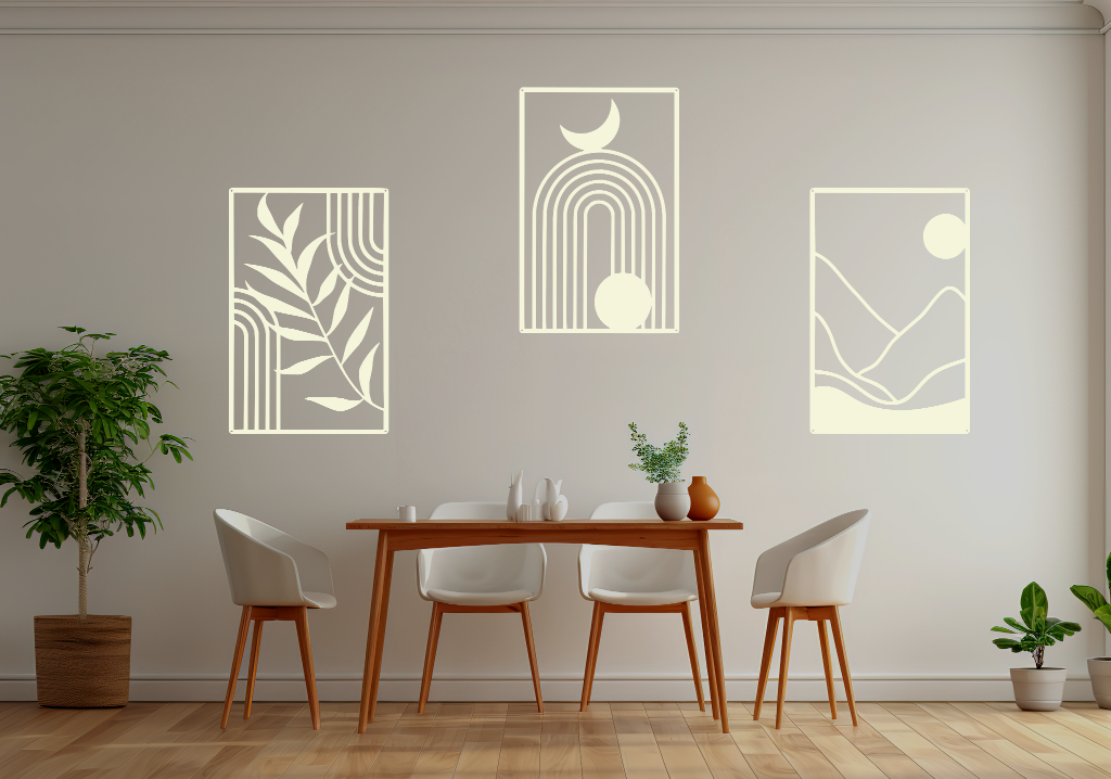 A three-piece minimalist geometric metal wall art set featuring abstract shapes, including a leaf design, a rainbow with moon and sun, and a mountain landscape, all finished in Canola Cream powder coating. The artwork is mounted on a dining room wall above a simple wooden table with white chairs, bringing a modern and artistic touch to the space.