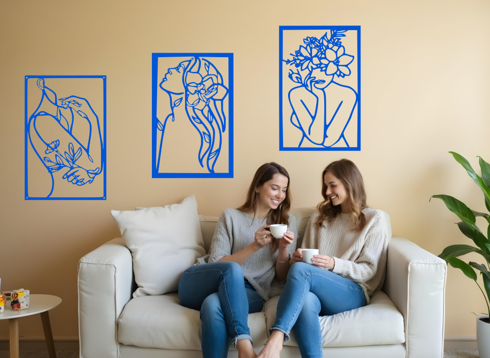 Set of three minimalist metal wall art pieces depicting floral-inspired female figures in various poses, finished in Blaze Blue Gloss powder coating, mounted on a neutral wall in a cozy living room setting where two women are enjoying coffee together.