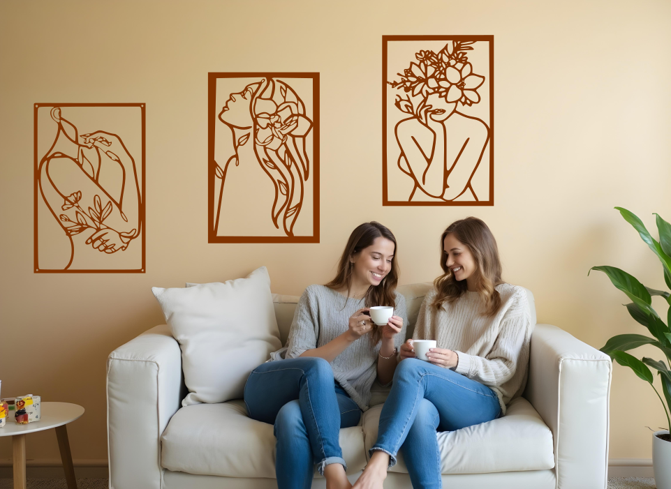 Set of three minimalist metal wall art pieces depicting floral-inspired female figures in various poses, finished in Rust Patina powder coating, mounted on a neutral wall in a cozy living room setting where two women are enjoying coffee together.