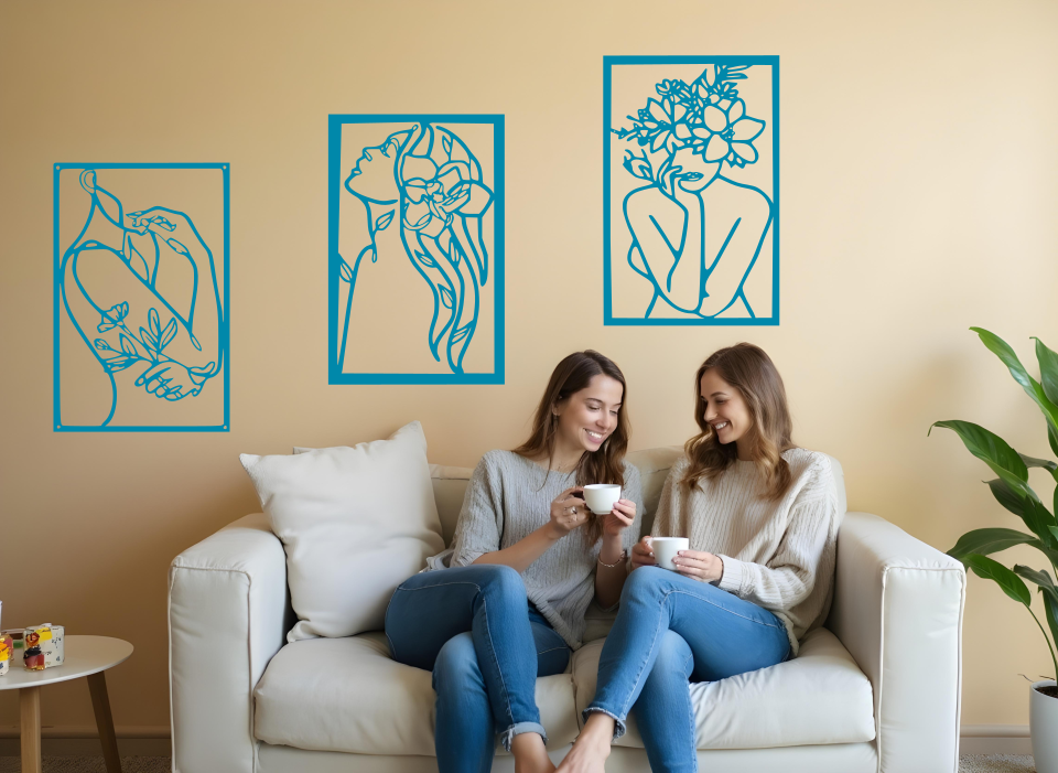 Set of three minimalist metal wall art pieces depicting floral-inspired female figures in various poses, finished in Wedgwood Satin powder coating, mounted on a neutral wall in a cozy living room setting where two women are enjoying coffee together.