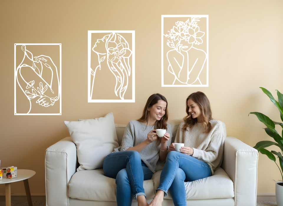 Set of three minimalist metal wall art pieces depicting floral-inspired female figures in various poses, finished in Bright White Gloss powder coating, mounted on a neutral wall in a cozy living room setting where two women are enjoying coffee together.