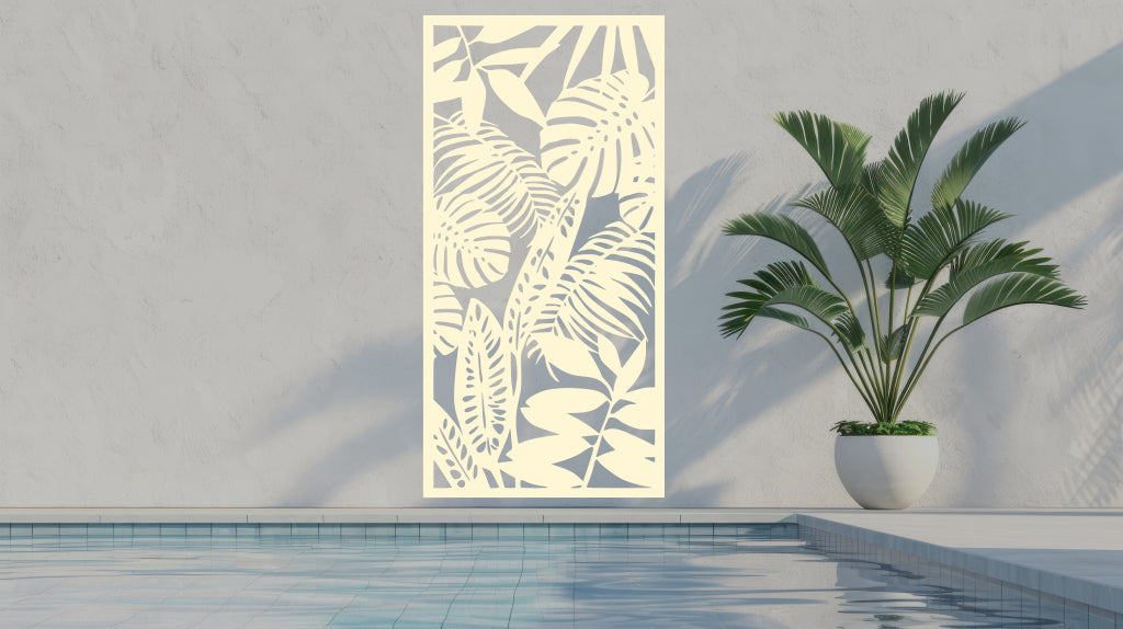 The 'Rainforest Leaves' metal privacy screen featuring an intricate design of tropical leaves, finished in Canola Cream powder coating. The screen is mounted on a white wall near a serene poolside area with a large potted plant, adding a soft and stylish touch to the outdoor space.