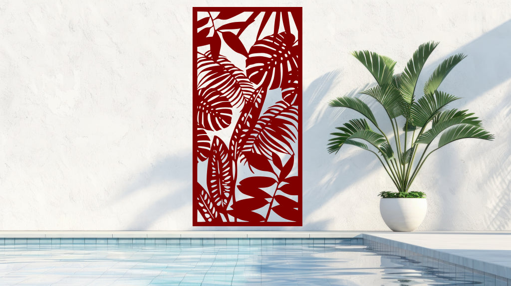 The 'Rainforest Leaves' metal privacy screen featuring an intricate design of tropical leaves, finished in Manor Red powder coating. The screen is mounted on a white wall near a serene poolside area with a large potted plant, adding a sophisticated and stylish touch to the outdoor space